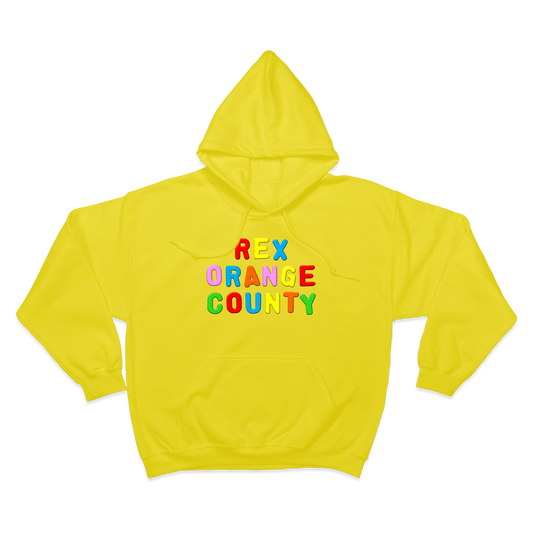 Front view of a yellow unisex regular-fit hoodie with a drawstring hood and front pocket, featuring a colourful ‘Rex Orange County’ text print across the front, with each letter in a different colour.